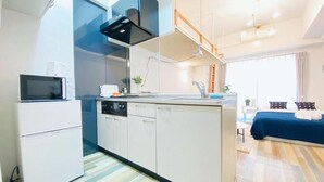 Eine kompakte Küche mit Mikrowelle, Herd und Spüle, ein kleiner Kühlschrank und ein blaues Sofa im angrenzenden Wohnbereich.