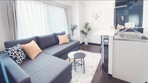 Ein modernes Wohnzimmer mit einer grauen Couch, einem kleinen runden Tisch und einer Küchenzeile mit Spüle und Arbeitsfläche.