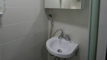 A bathroom with white tiles, a sink, a mirror, and a shower.