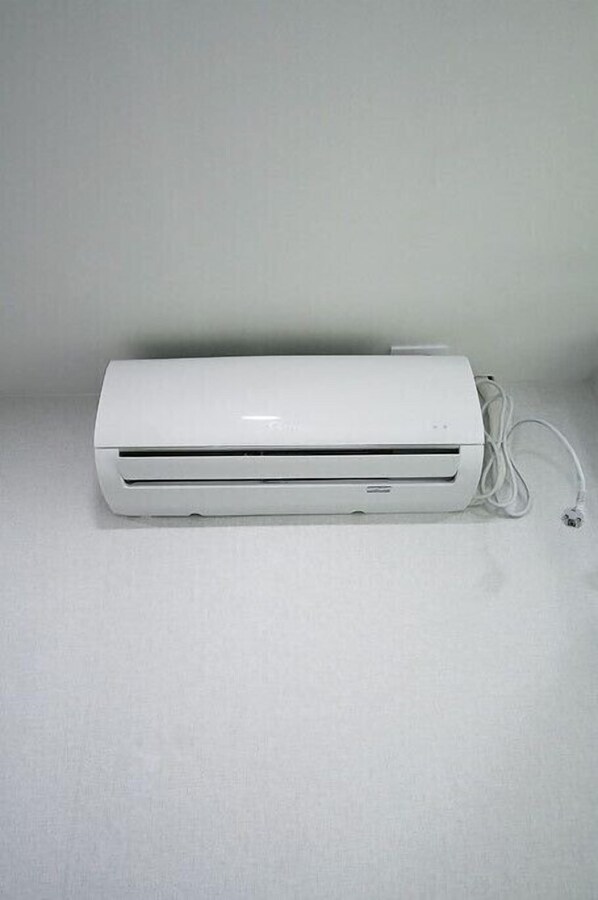 A white portable air conditioner with a power cord, placed on a plain surface. - Anam House (Seoul)