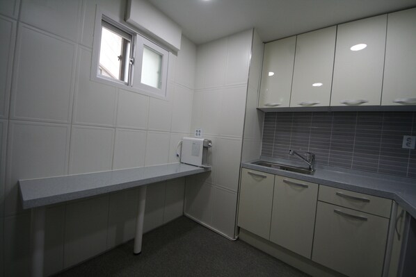A compact kitchen with white cabinets, a grey countertop, a window, and a sink. - Anam House (Seoul)