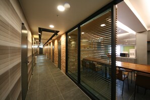 A modern hotel corridor with a long hallway, wooden walls, and a dining area with tables and chairs. - Anam House (Seoul)