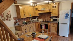 Una cocina con armarios de madera, una mesa de comedor con sillas, un refrigerador y un microondas.