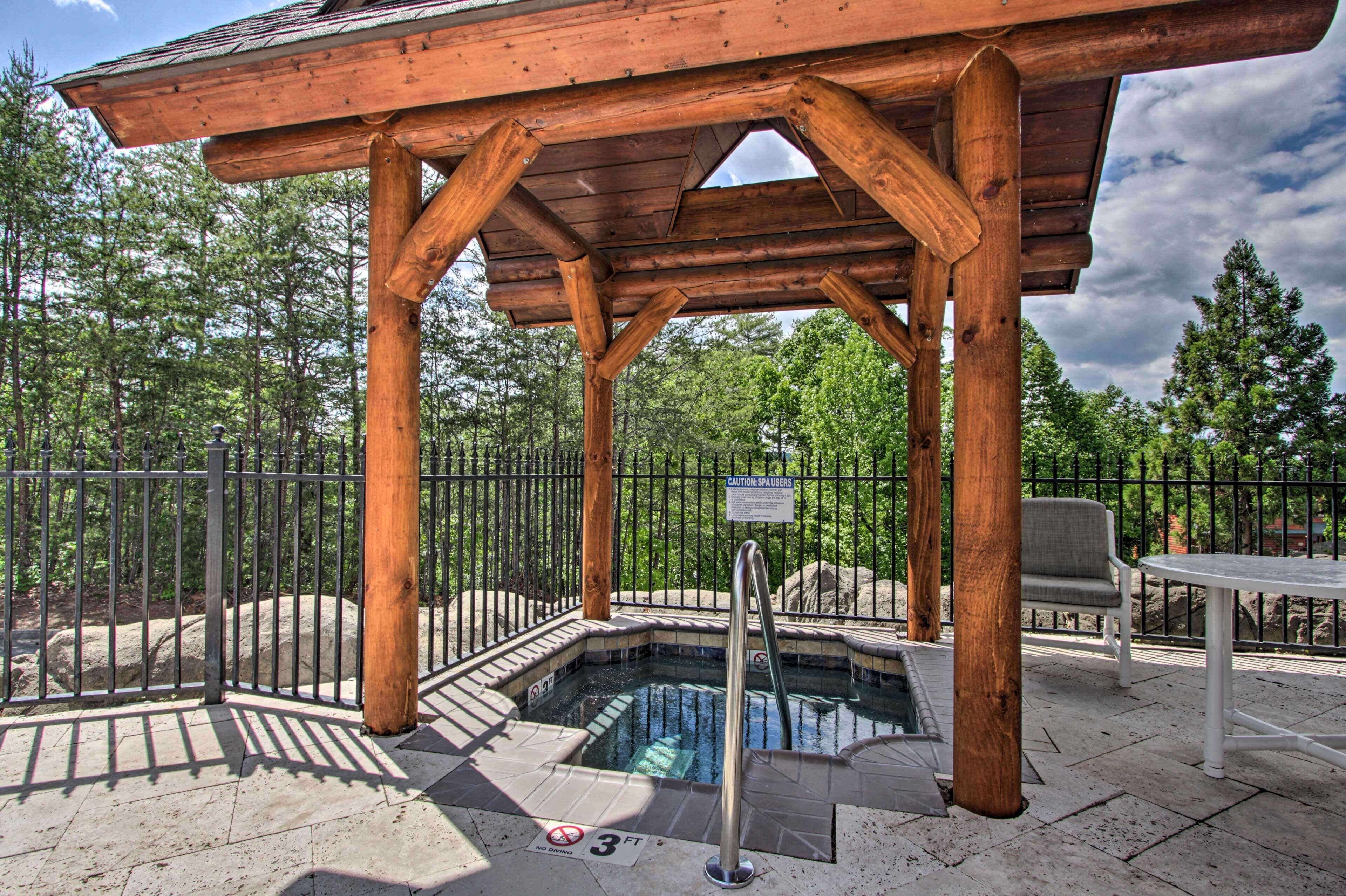A wooden gazebo with a hot tub, surrounded by a metal fence and trees.
