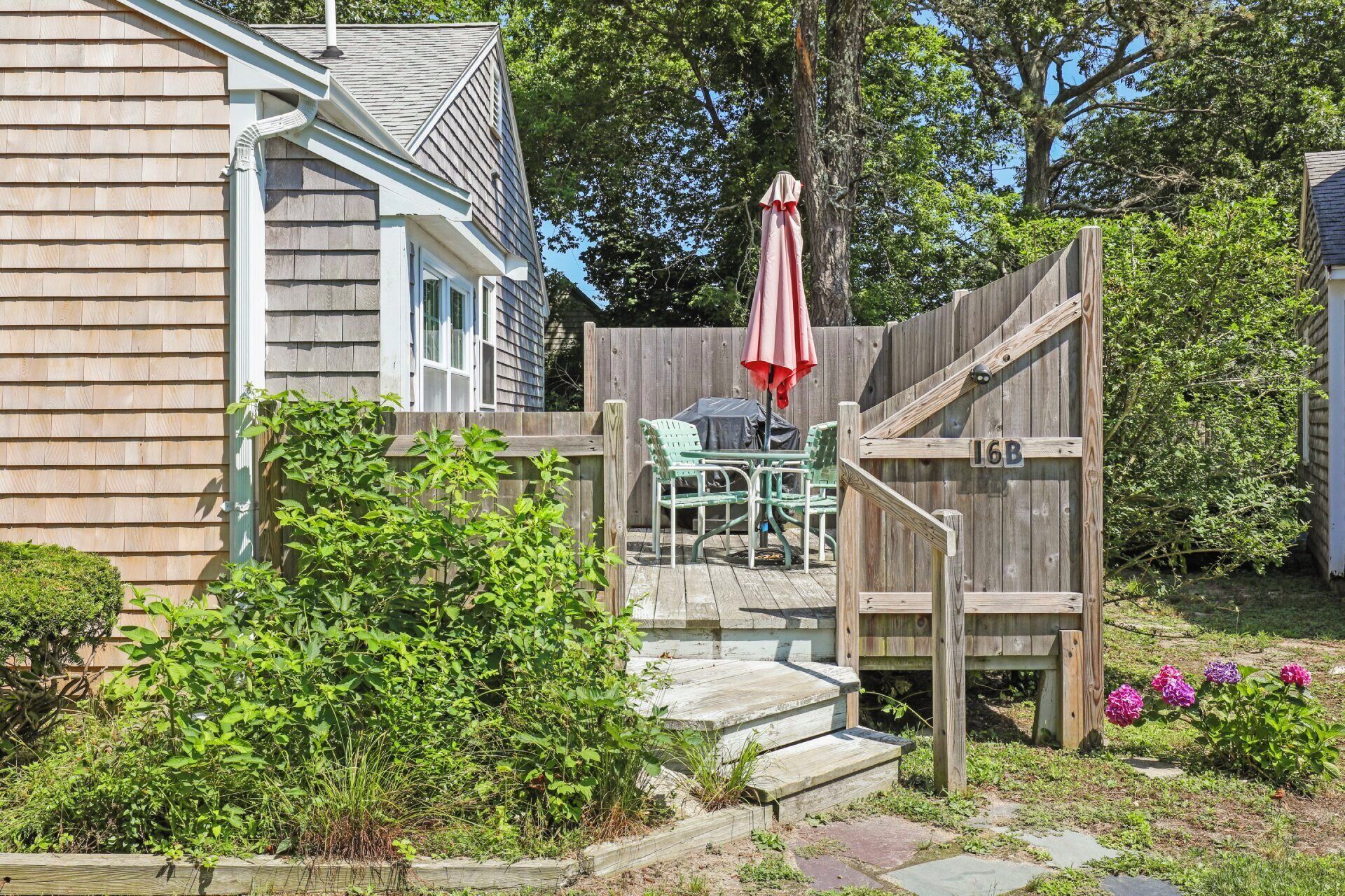 A wooden deck with a covered table and chairs, a wooden fence with a gate, and a mailbox marked "16B".