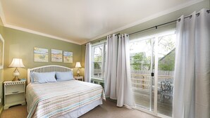 A bedroom with a bed, two bedside tables with lamps, a window with curtains, and artwork on the wall.