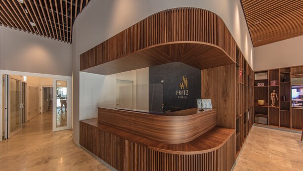 A reception desk with a curved wooden design, a black sign with 'Fritz Tower' text, and a glass door leading to a hallway. - FRITZTOWER - Apartment (Mitte)