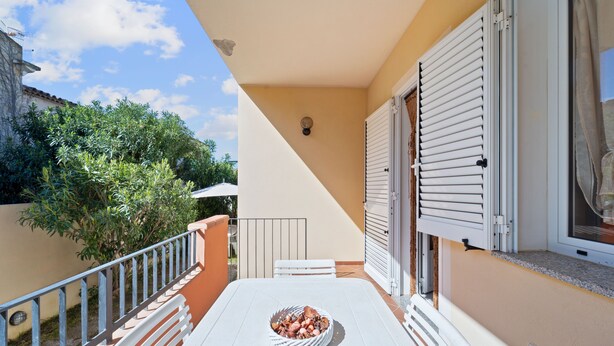 Un balcon avec une table, un panier de fruits et une fenêtre avec des volets.