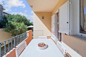 Un balcón con una mesa, un frutero y una ventana con contraventanas.