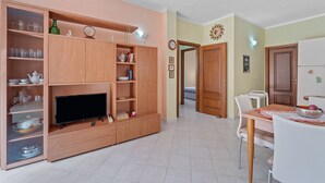 Un salon comprenant un téléviseur, un meuble en bois, une table à manger et des chaises.