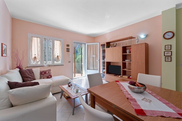 Una sala de estar con un sofá, una mesa de comedor, un televisor y una estantería.