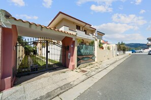 Edificio residencial con entrada protegida por una verja, camino de acceso pavimentado y vista a la calle.