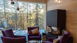 A modern interior with wooden walls, large windows, and a fireplace. There are purple armchairs and a wooden coffee table. - Arctic Skylight Lodge (Muonio)