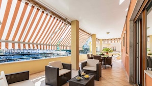A balcony with wicker furniture, a dining table, and a view of a pool and buildings. - Modern spacious apartment with terrace, balconies, solarium & gym (Sorrento)