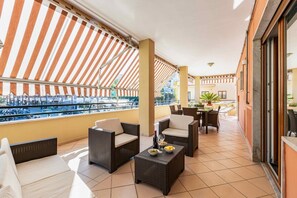 A balcony with wicker furniture, a dining table, and a view of a pool and buildings.