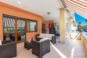 Un balcon agrémenté de meubles en osier, une porte vitrée donnant sur un espace extérieur et un auvent à rayures.