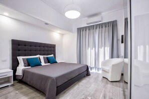 A modern bedroom with a large bed, a white nightstand, a desk, and a chair.