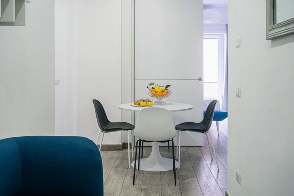 A small dining area with a white table, two black chairs, and a bowl of fruit on the table.
