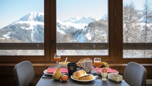 Una mesa de desayuno con vista a la montaña, que incluye un croissant, fruta y bebidas.