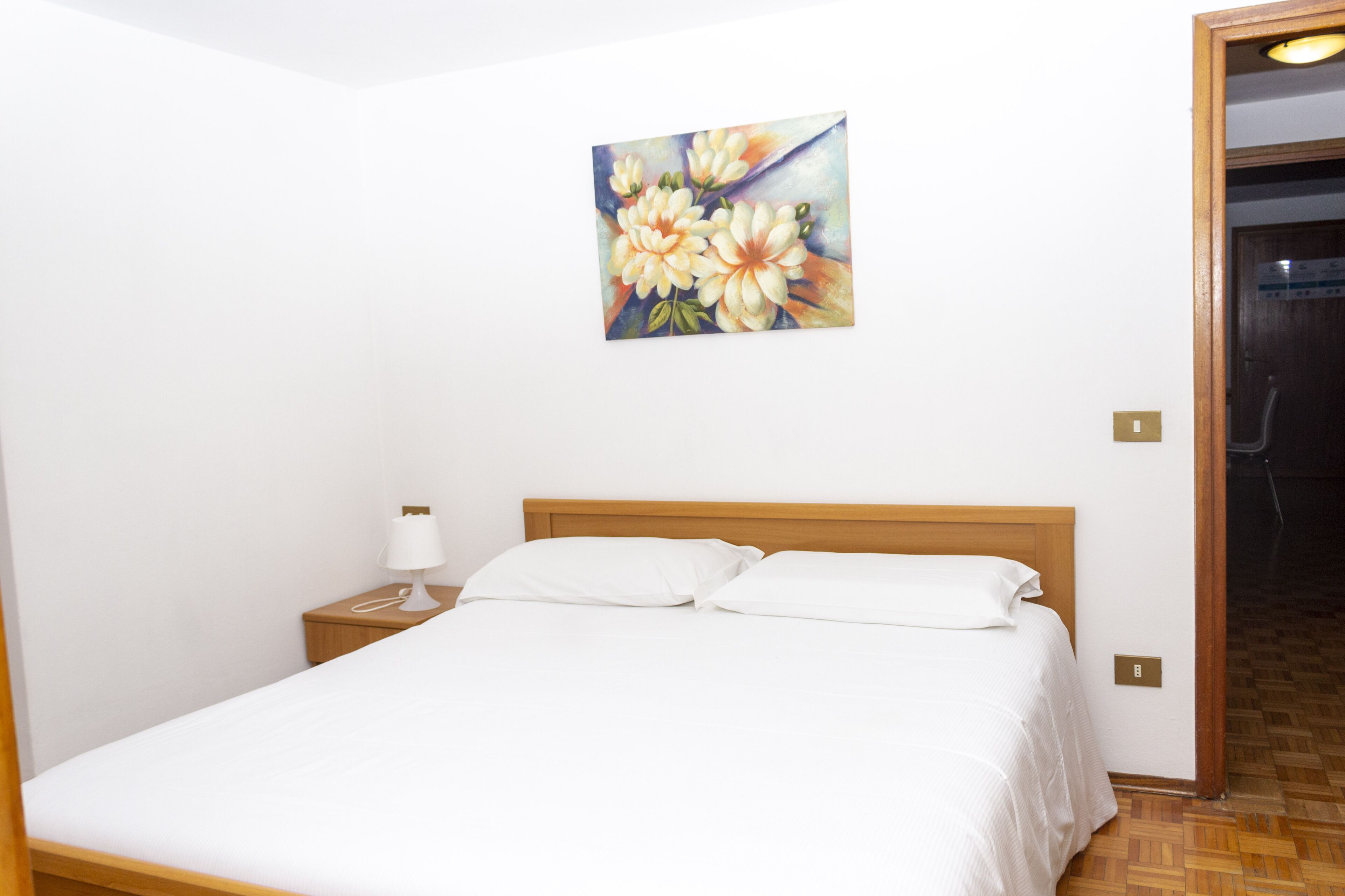 A neatly made bed with white linens, a wooden headboard, and a bedside table with a lamp.