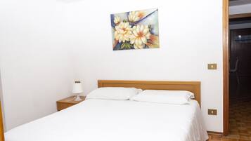 A neatly made bed with white linens, a wooden headboard, and a bedside table with a lamp.