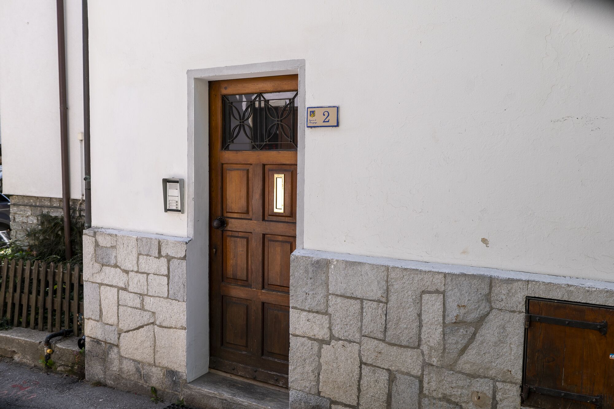 A wooden door with a window above it, a stone wall, and a small sign with the number 2.