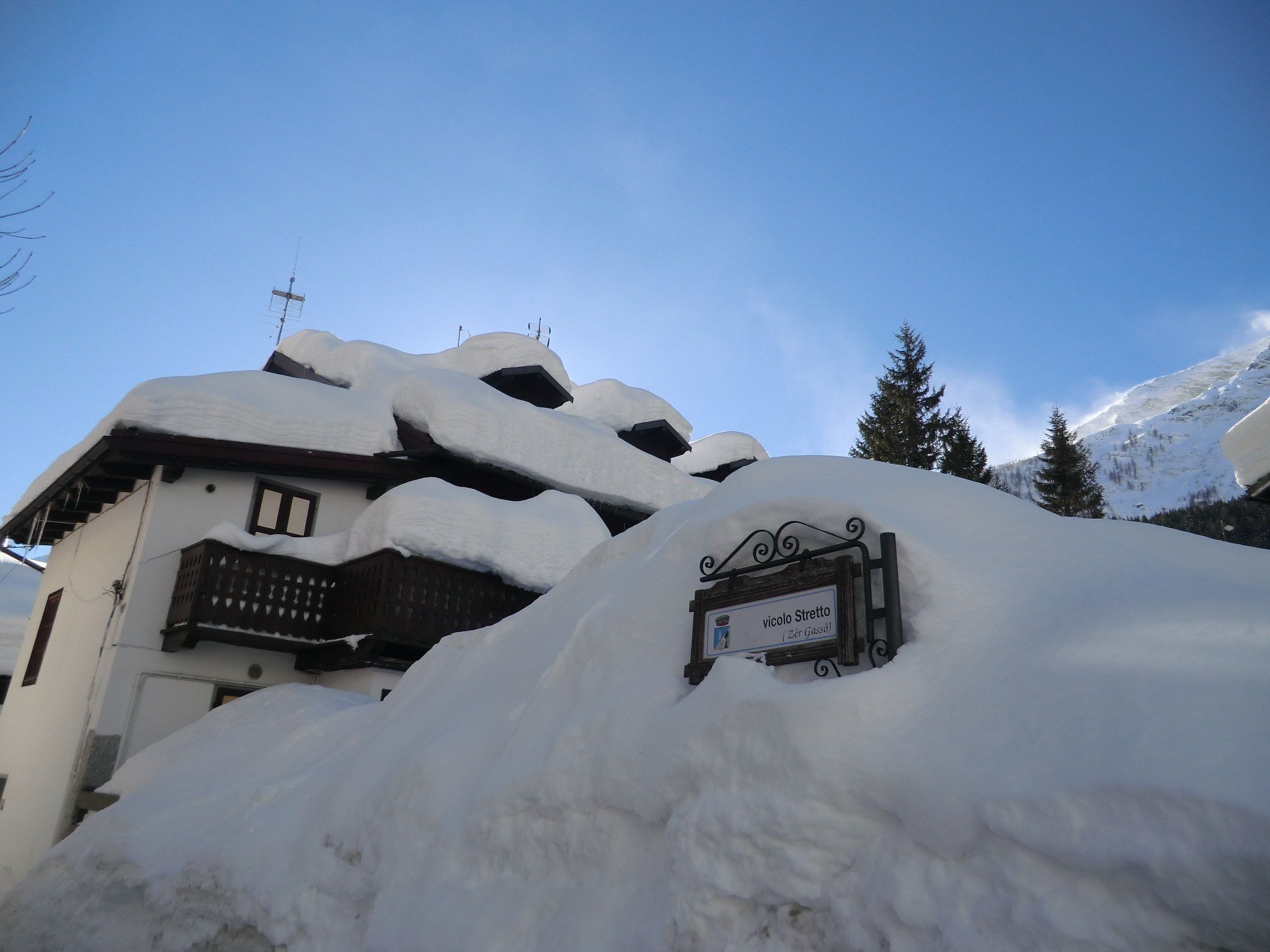 A snow-covered building with a sign indicating 'vicolo stretto' and 'Zur Güssam'.
