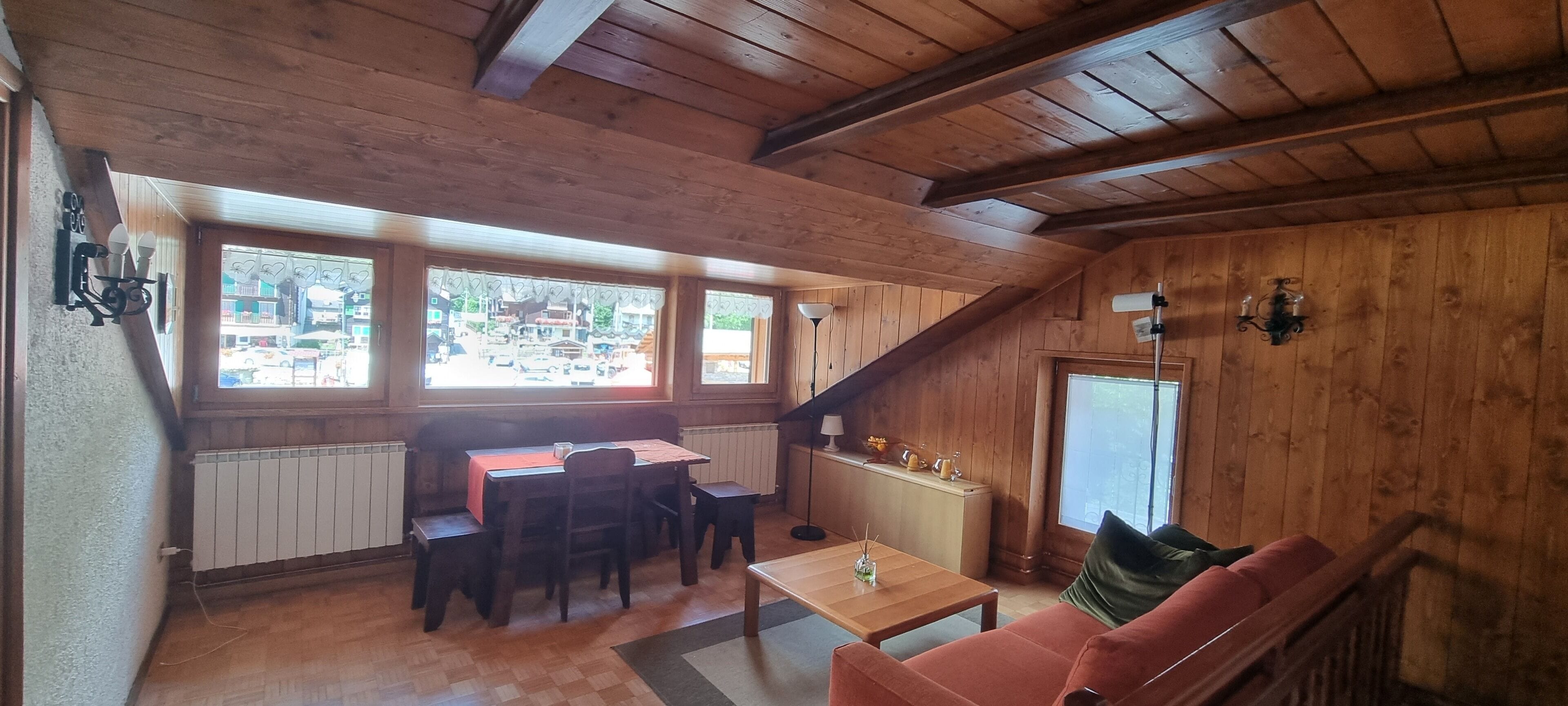 Ein gemütliches Zimmer mit Holzwänden und geneigter Decke, mit Essbereich, Tisch und Stühlen, einer Couch und einer kleinen Küchenzeile mit Arbeitsfläche und Spüle.
