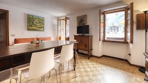 Un comedor con una mesa de madera, sillas blancas, un televisor y una ventana con vistas a edificios.