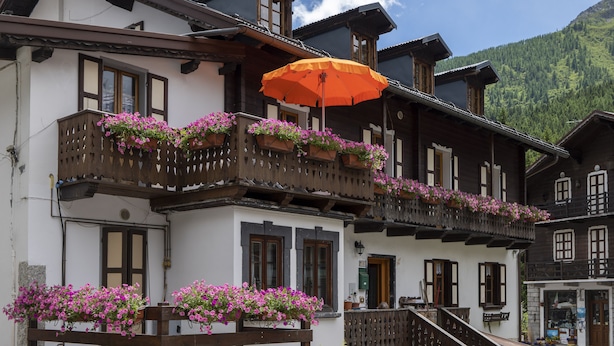 Una cabaña tradicional con balcones decorados con flores, barandillas de madera y vistas despejadas de las montañas circundantes.