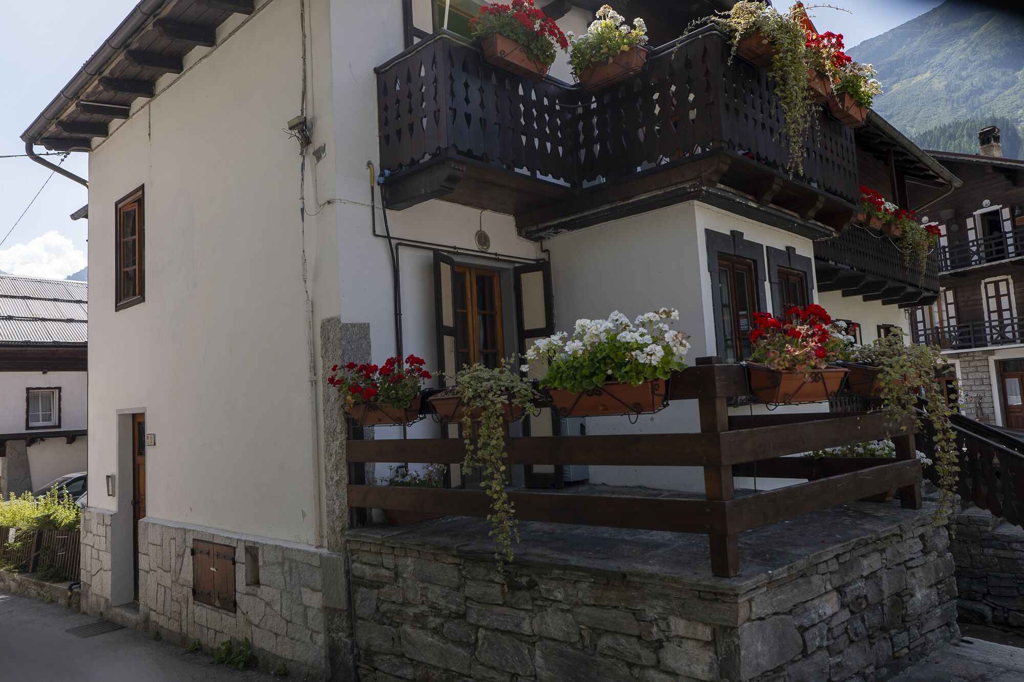Ein traditionelles Gebäude mit steinernen Fundament, hölzernen Balkonläufungen und Blumenkästen am Balkon.