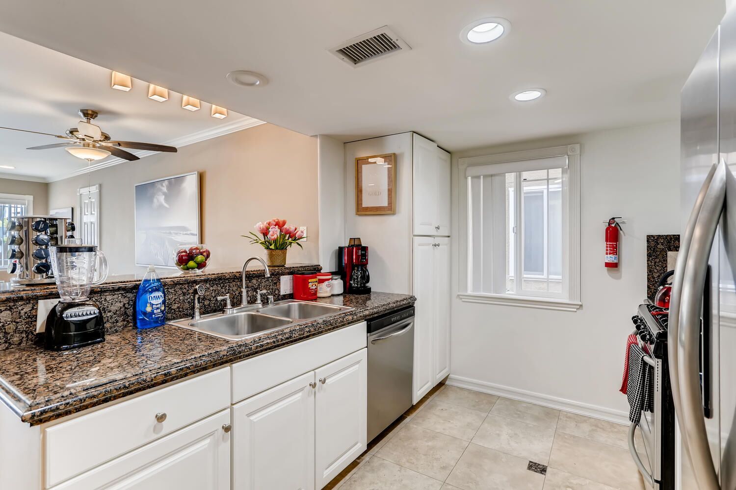 A modern kitchen with granite countertops, white cabinetry, a built-in dishwasher, and a stainless steel refrigerator.