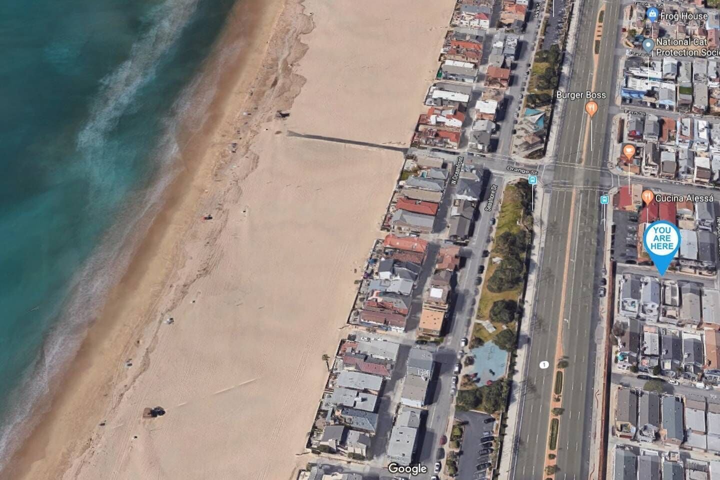 An aerial view of a coastal town with a beach, roads, and buildings.