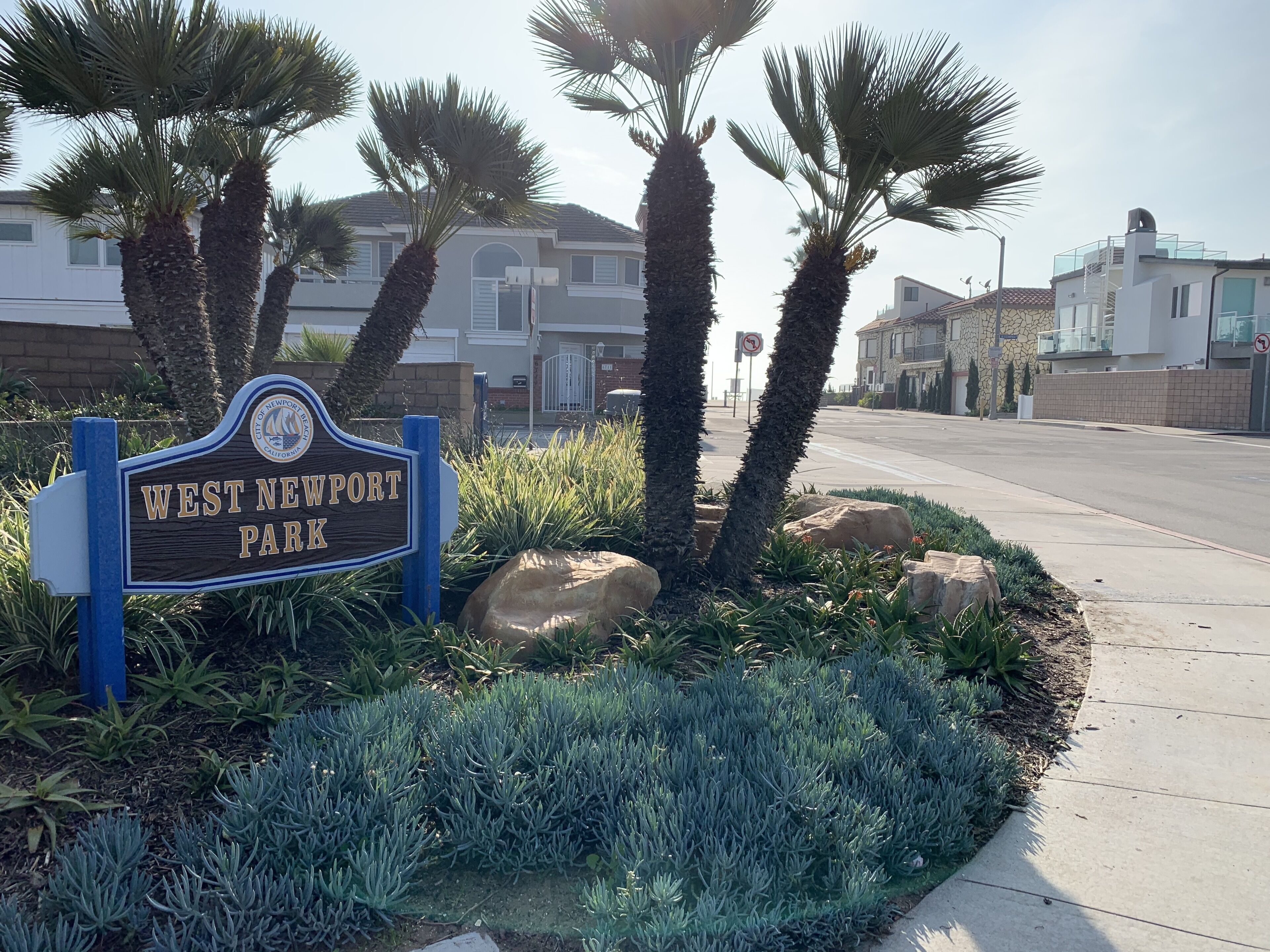 A sign for West Newport Park with a clear sky and residential buildings in the background.
