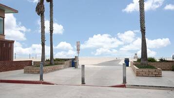 A beachside walkway with palm trees, a trash bin, and a lifeguard tower in the distance.