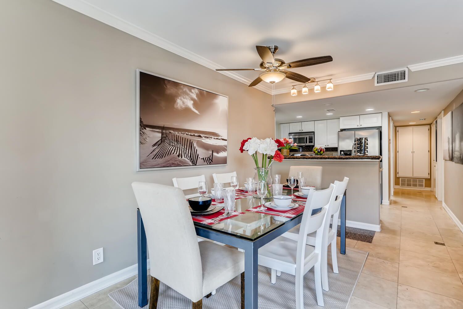 A dining area with a glass table, white chairs, and a ceiling fan.