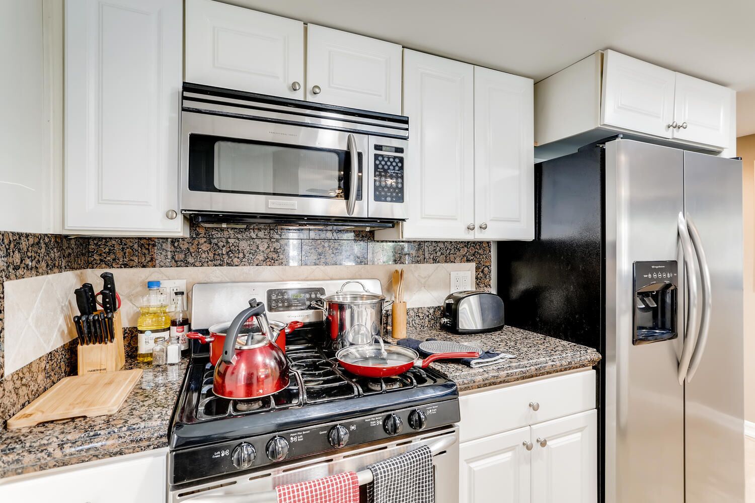 Una cocina con gabinetes blancos, un refrigerador de acero inoxidable, un microondas, una estufa y un tostador.