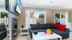 A living room with a grey sofa, red cushions, a white coffee table, and a flat-screen TV mounted on the wall. - Costa Mesa/Newport - Fast WiFI - Work Stations - Free Parking - Self Check In! (CM-1) (Costa Mesa)