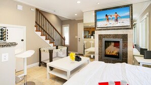 A hotel room with a fireplace, a television mounted above it, a bed, a dining area with a table and chairs, and a kitchen area visible through an open door. - Costa Mesa/Newport - Fast WiFI - Work Stations - Free Parking - Self Check In! (CM-1) (Costa Mesa)