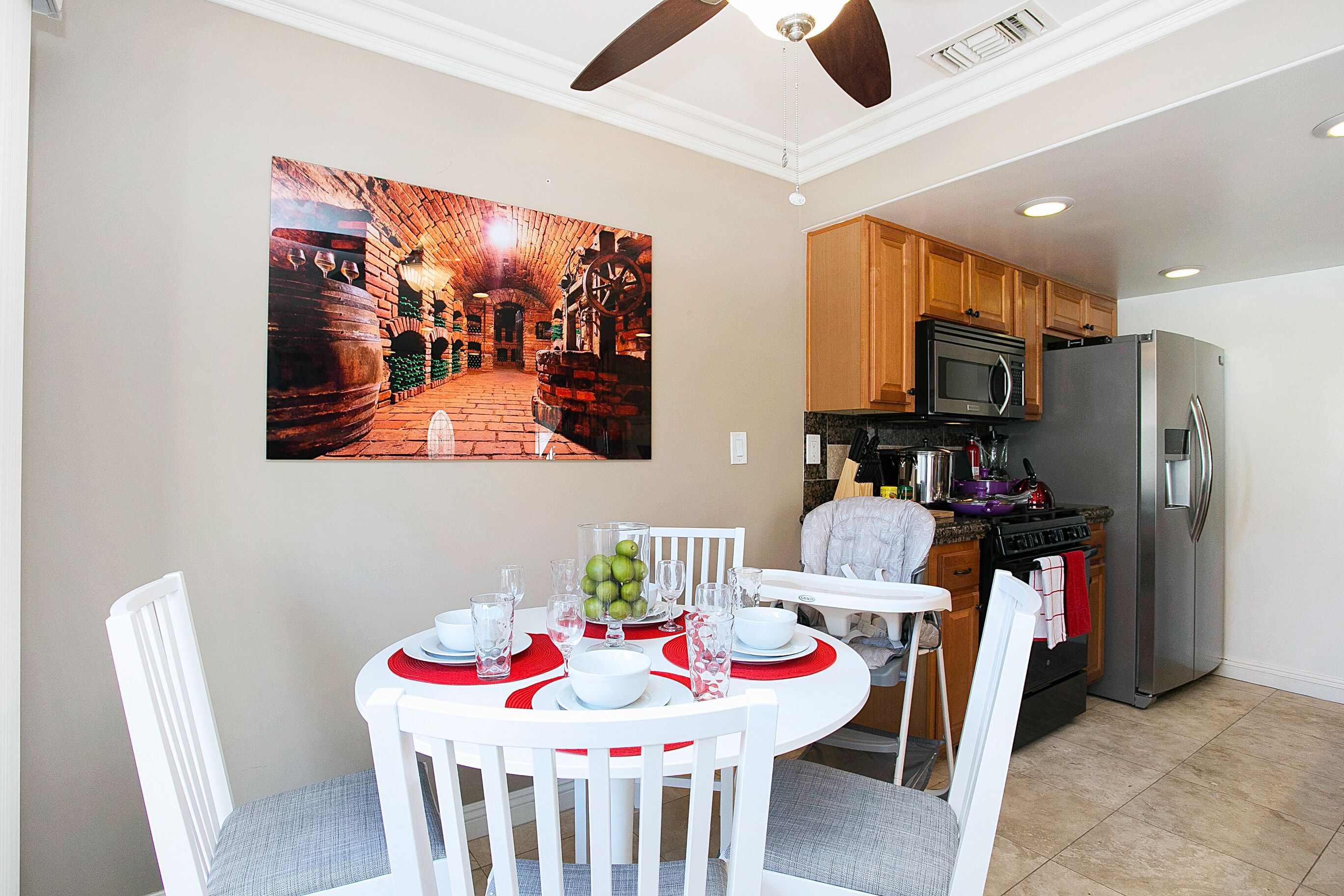 A dining area with a table set for four, a kitchen with modern appliances, and a large painting on the wall.