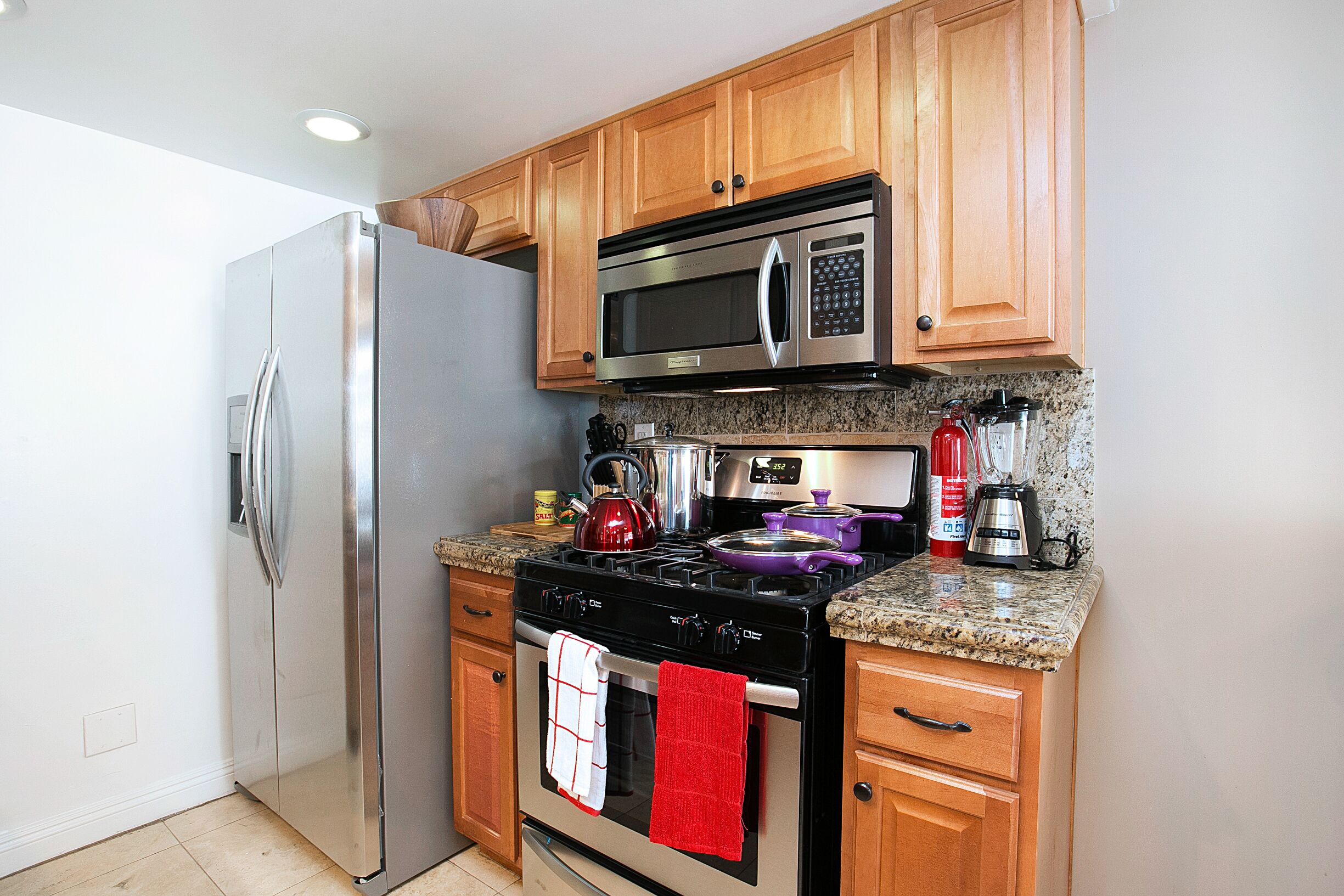 A kitchen with wooden cabinets, stainless steel appliances, granite countertops, and a red towel hanging on the oven handle.