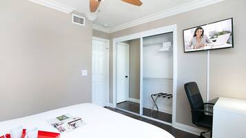A modern room with a white desk, a red tray, a black office chair, a ceiling fan, and a TV on the wall.