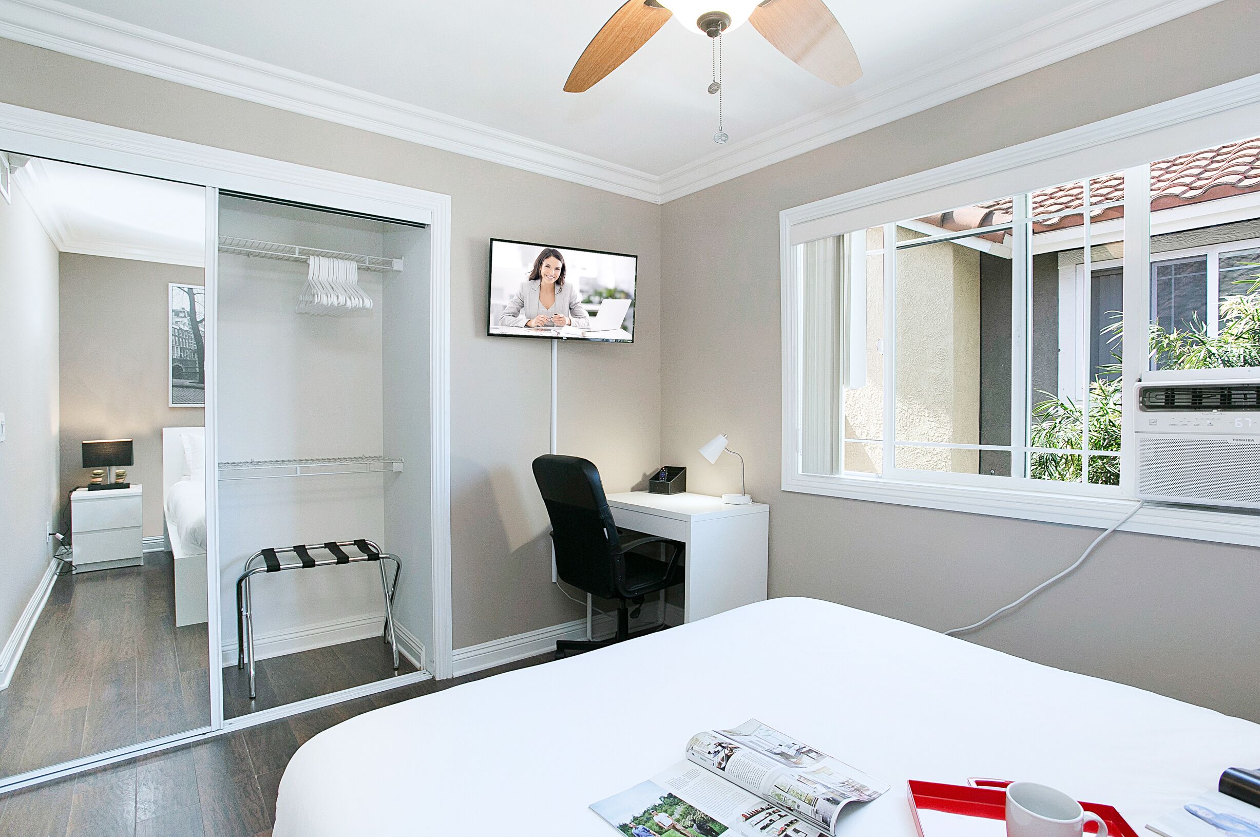 Habitación de hotel con cama, escritorio, silla, televisión, ventana con aire acondicionado y puerta corredera que da al baño.