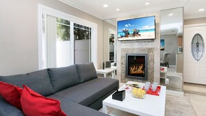 A modern living room with a grey sofa, red cushions, a flat-screen TV, a fireplace, and a dining area with a white table and chairs. - Awesome Multi Level - Large Patio - Fast WIFI - Work Desks - Self Check In! (CM-2) (Costa Mesa)
