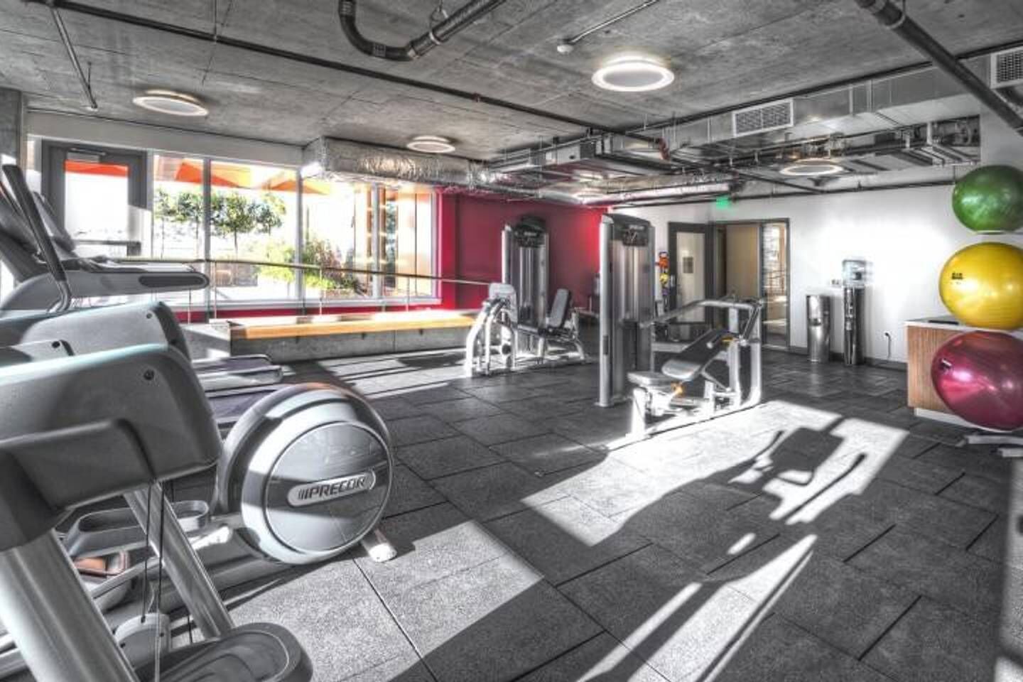 A gym with exercise equipment, a red wall, and large windows.