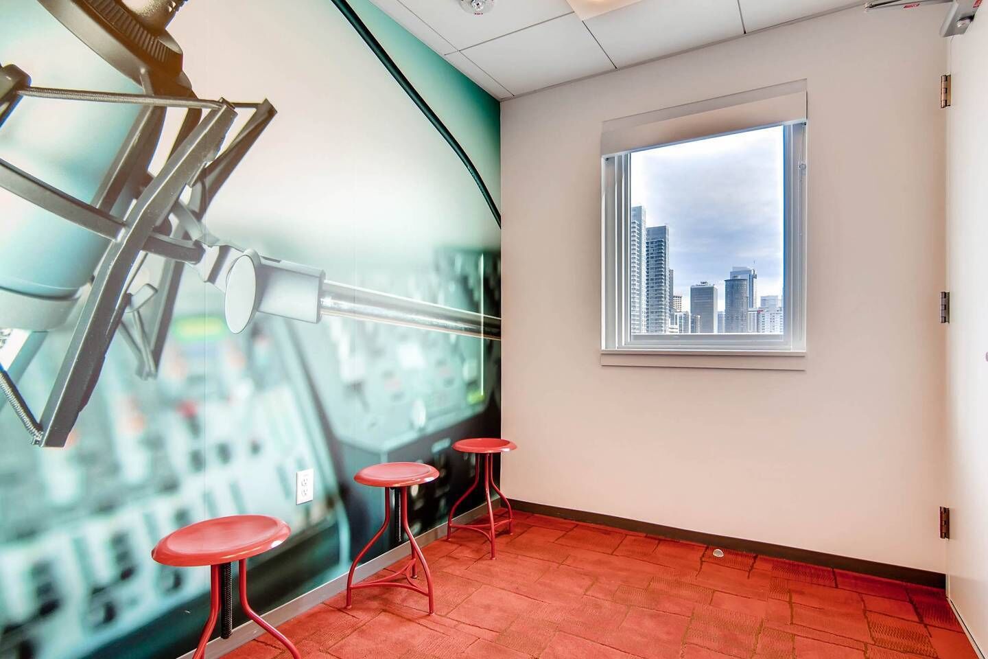 A room with a large window, red stools, and a wall mural of a cityscape.
