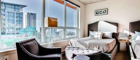 Ein modernes Hotelzimmer mit großem Fenster, einem Bett, einem Sessel und einem kleinen Tisch.