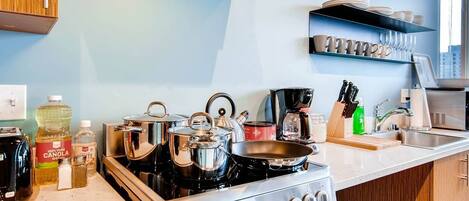 Une cuisine moderne équipée d’appareils électroménagers en acier inoxydable, notamment une cuisinière, des casseroles et une machine à café. Des étagères au-dessus du plan de travail servent à ranger la vaisselle et les verres.
