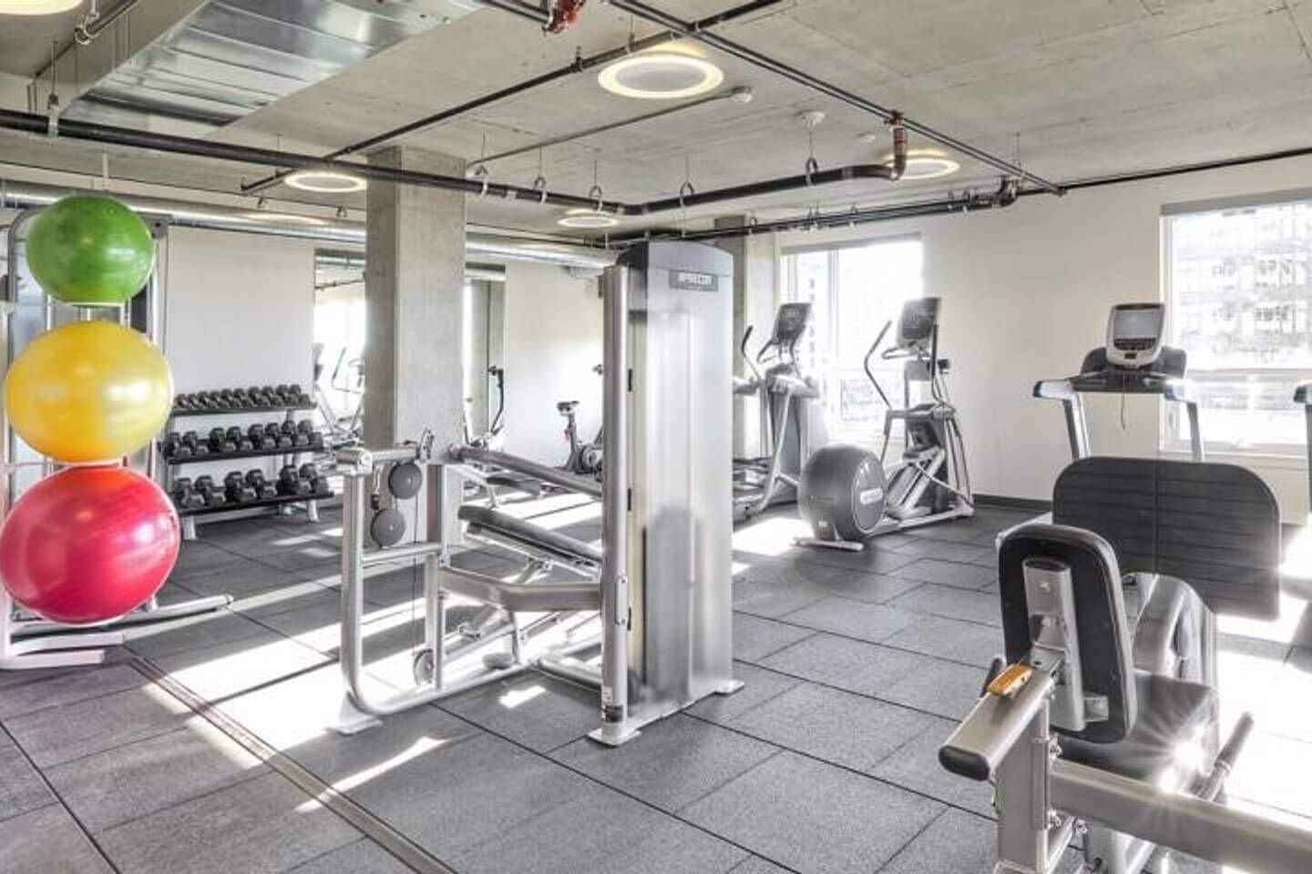 Et fitnessrum med træningsudstyr, vægtstativer og et løbebånd.