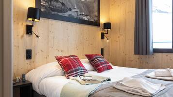 A neatly made bed with plaid pillows, a bedside table with a lamp, and a framed picture on the wall.